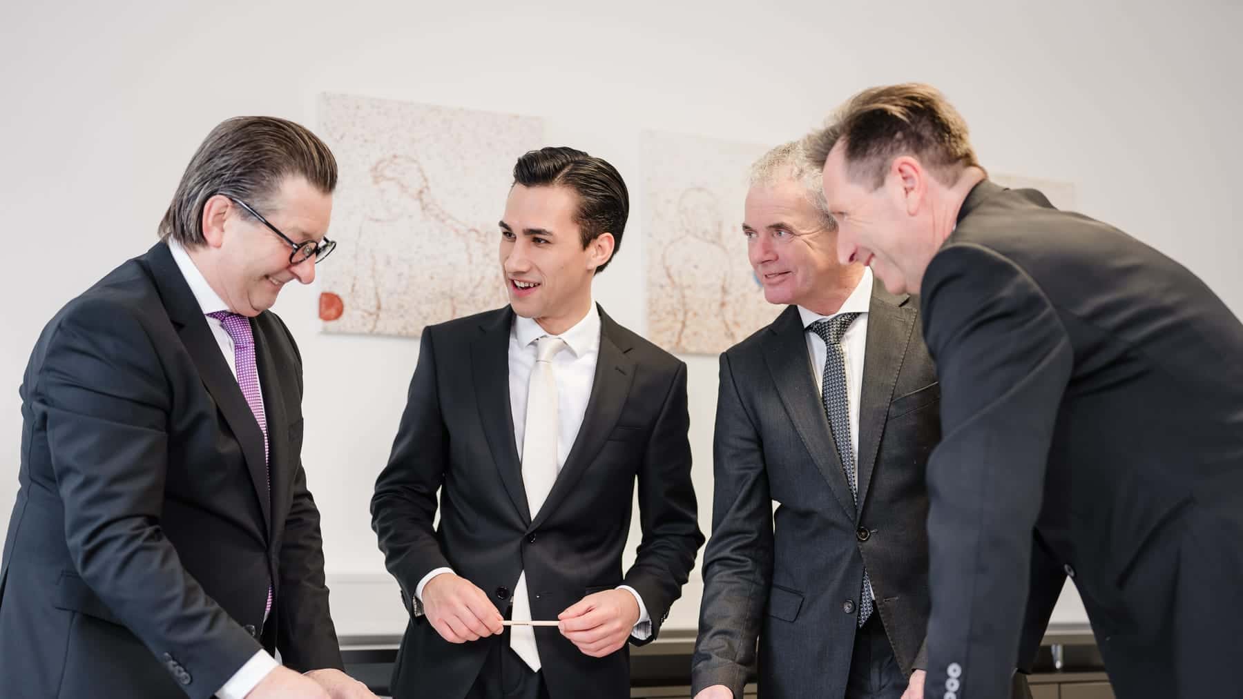 Vier Männer besprechen Pläne am Tisch — Projektgespräch zu einer Gewerbeimmobilie